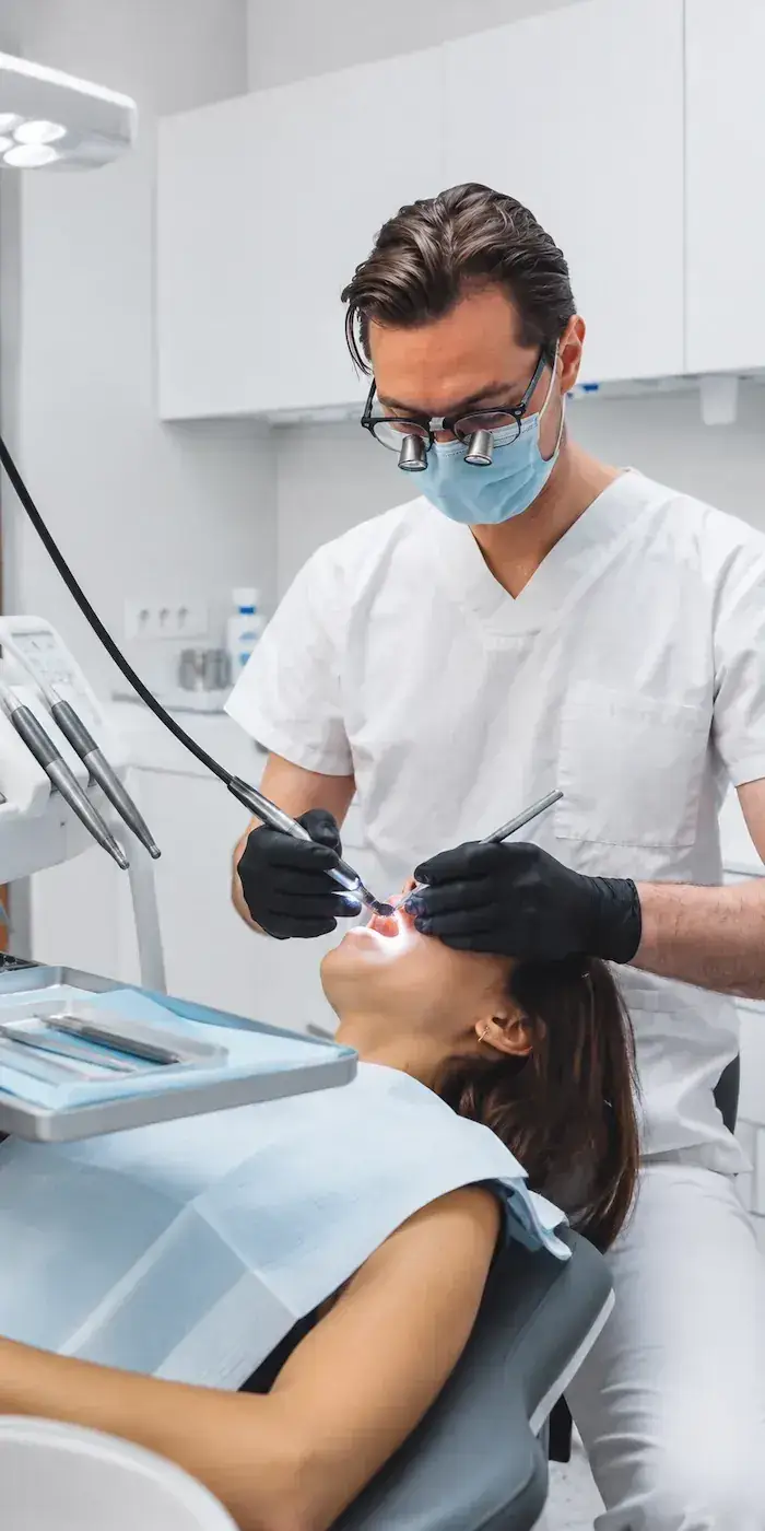 Dentist in a white coat and mask treating a patient reclined in a clinic chair.