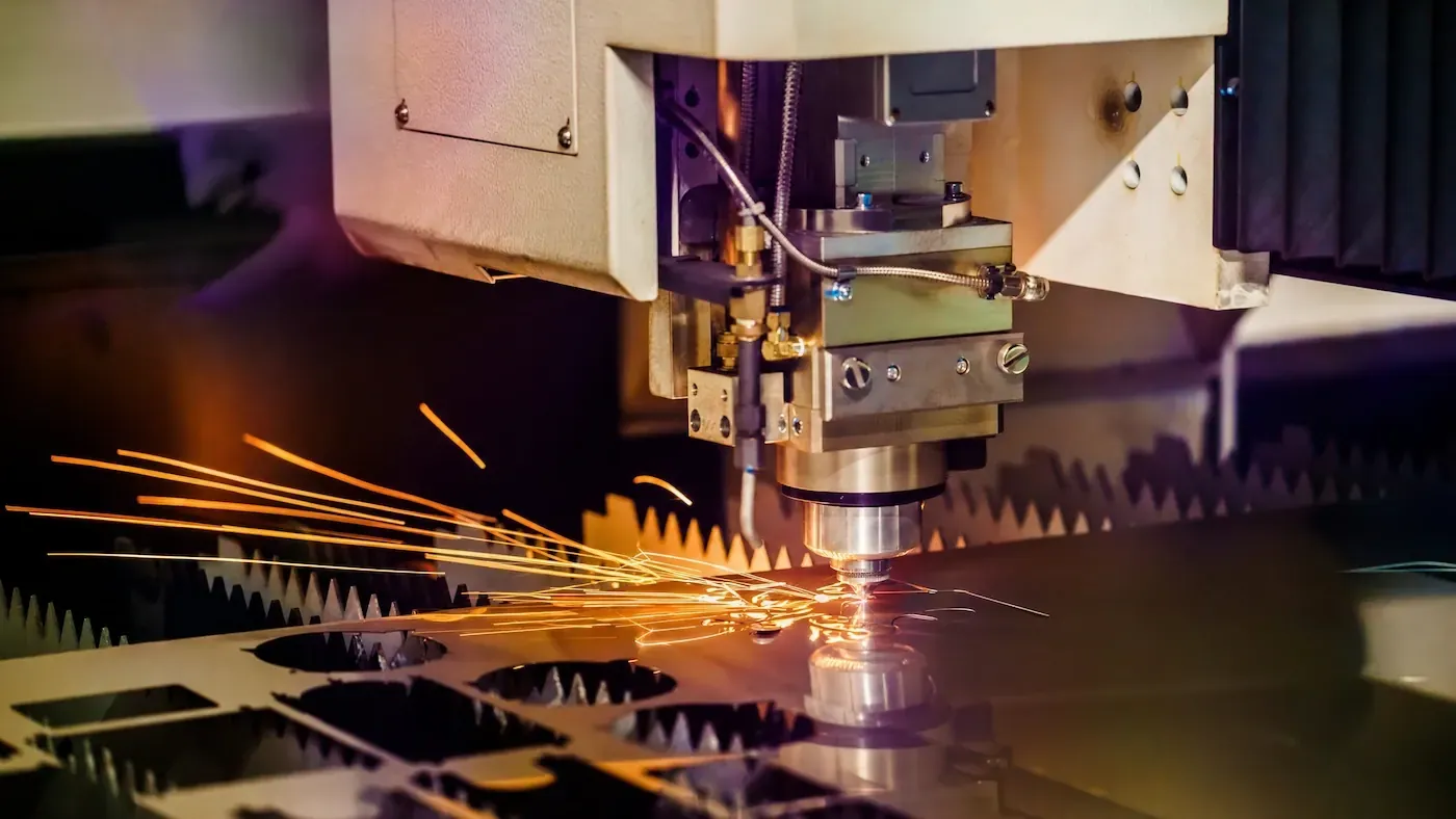 CNC cutting head sending orange sparks across a metal plate on a shop floor.