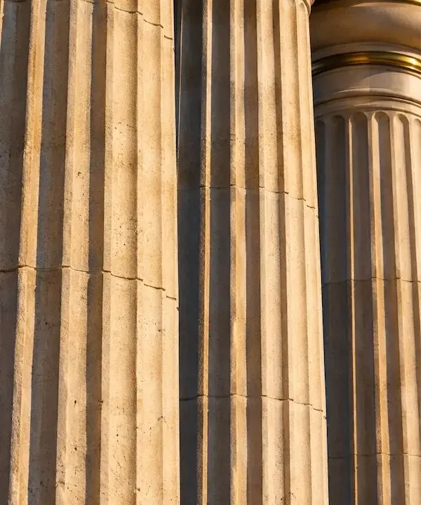 Close crop of fluted limestone columns banded in brass, lit by low gold sunlight.